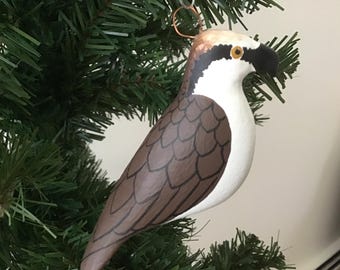 May include: A hand-painted bird ornament with a brown, white, and black design. The bird has a detailed feather pattern on its wings and is hanging from a copper-colored wire. The ornament is displayed on a green Christmas tree.
