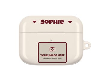 Op de afbeelding: Een crèmekleurig beschermhoesje voor draadloze oordopjes met de naam SOPHIE in donkerrode tekst, geflankeerd door twee kleine hartjes. Onder de naam staat een rechthoekige tijdelijke aanduiding met een camerapictogram en de tekst YOUR IMAGE HERE.