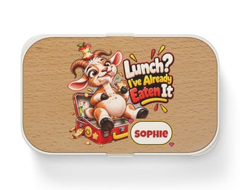 Könnte beinhalten: Eine rechteckige Brotdose mit heller Holzmaserung, die eine Cartoon-Ziege zeigt, welche in einer offenen roten Brotdose sitzt. Der Text lautet Lunch? I've Already Eaten It und der Name SOPHIE steht in einem weißen Oval mit gelbem Rand.