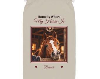 Könnte beinhalten: Ein beigefarbener Beutel mit Kordelzug und dem Text "Home Is Where My Horse Is" in dunkelbrauner und kastanienbrauner Schrift. Darunter befindet sich ein gerahmtes Foto eines braunen Pferdes mit weißer Blesse, dem Namen "Biscuit" und zwei Herzen.