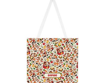 Op de afbeelding: Een witte tote bag met een herhalend patroon van cartoongeitjes, rode appels, oranje wortels, sapverpakkingen en sandwiches. Een rechthoekig label onderaan in het midden toont de naam SOPHIE in dikgedrukte, donkerrode hoofdletters op een crème achtergrond.