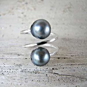May include: A silver ring with two dark gray pearls. The ring is twisted and the pearls are set on top of the twist.