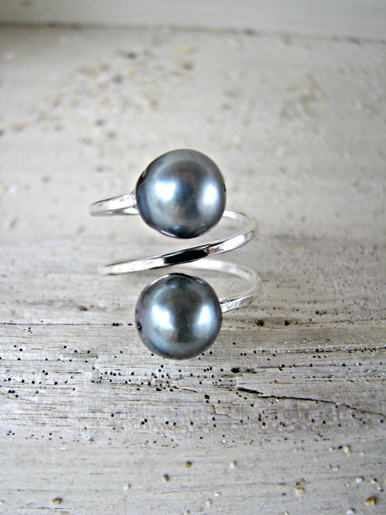May include: A silver ring with two dark gray pearls. The ring is twisted and the pearls are set on top of the twist.