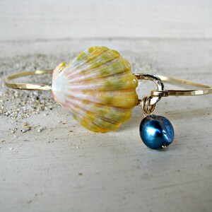 Puede incluir: Un brazalete de oro con un dije de concha amarilla y rosa y una perla azul oscuro colgante.