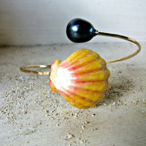 May include: A gold bangle bracelet with a black pearl and a yellow seashell. The bracelet is open and the pearl is on the end of the wire.
