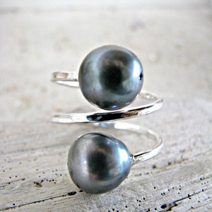 May include: A silver ring with two dark gray pearls. The ring is twisted and the pearls are set on the top of the ring.