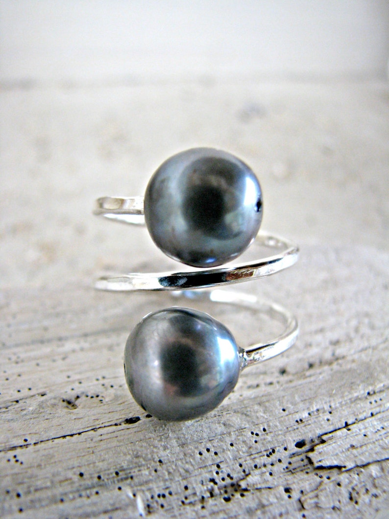 May include: A silver ring with two dark gray pearls. The ring is twisted and the pearls are set on the top of the ring.