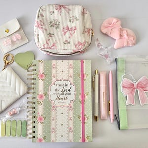 May include: A collection of stationery and accessories including a spiral-bound notebook with the text Trust in the Lord with all your Heart, a floral bow print pouch, a white quilted coin purse, pens, sticky tabs, and various bow-themed items.