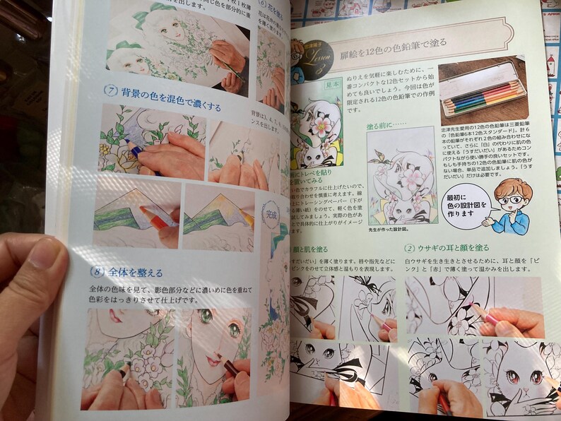 May include: A book page with illustrations and instructions for coloring. The page features step-by-step guides with images of hands coloring drawings of anime-style characters with colored pencils. Text in Japanese accompanies the images.