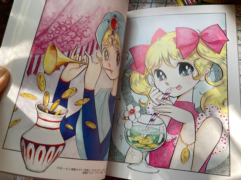 May include: A colorful illustration from a book featuring two anime-style characters. One character is playing a golden horn, with coins falling into a decorative vase. The other character is drinking from a glass with coins inside.