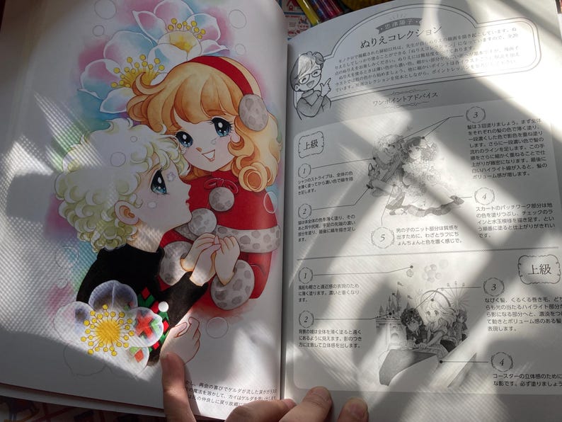 May include: A colorful illustration from a coloring book features two anime-style characters embracing. One has blonde hair and wears a black sweater, while the other has red hair and a red outfit. The background includes flowers and text.