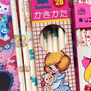 Puede incluir: Una colecci&oacute;n de l&aacute;pices y cajas de l&aacute;pices vintage. Los l&aacute;pices son blancos con ilustraciones de dibujos animados de cachorros y ni&ntilde;as. Las cajas de l&aacute;pices son rosas y presentan texto japon&eacute;s e ilustraciones de una ni&ntilde;a sosteniendo un cachorro.