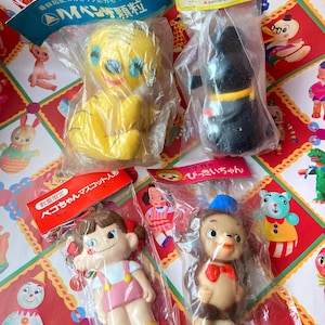 May include: Four vintage Japanese soft vinyl figures in original plastic packaging. The set includes a yellow tiger, a black animal bank, a girl with brown hair in a pink outfit, and a brown monkey character wearing a blue hat and red bow tie.
