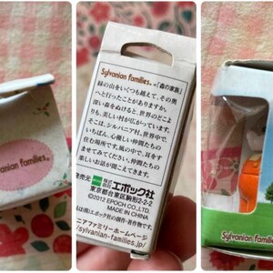 May include: A set of Sylvanian Families miniature figurines in their original packaging. The boxes feature text in Japanese and English, with a pink oval logo. One box shows a small orange figure.