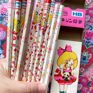 Puede incluir: Un conjunto de l&aacute;pices vintage con gomas rojas y barriles blancos decorados con dise&ntilde;os florales y de chicas de dibujos animados. Los l&aacute;pices est&aacute;n en una caja rosa con una ilustraci&oacute;n de dibujos animados de una ni&ntilde;a sosteniendo un panda.
