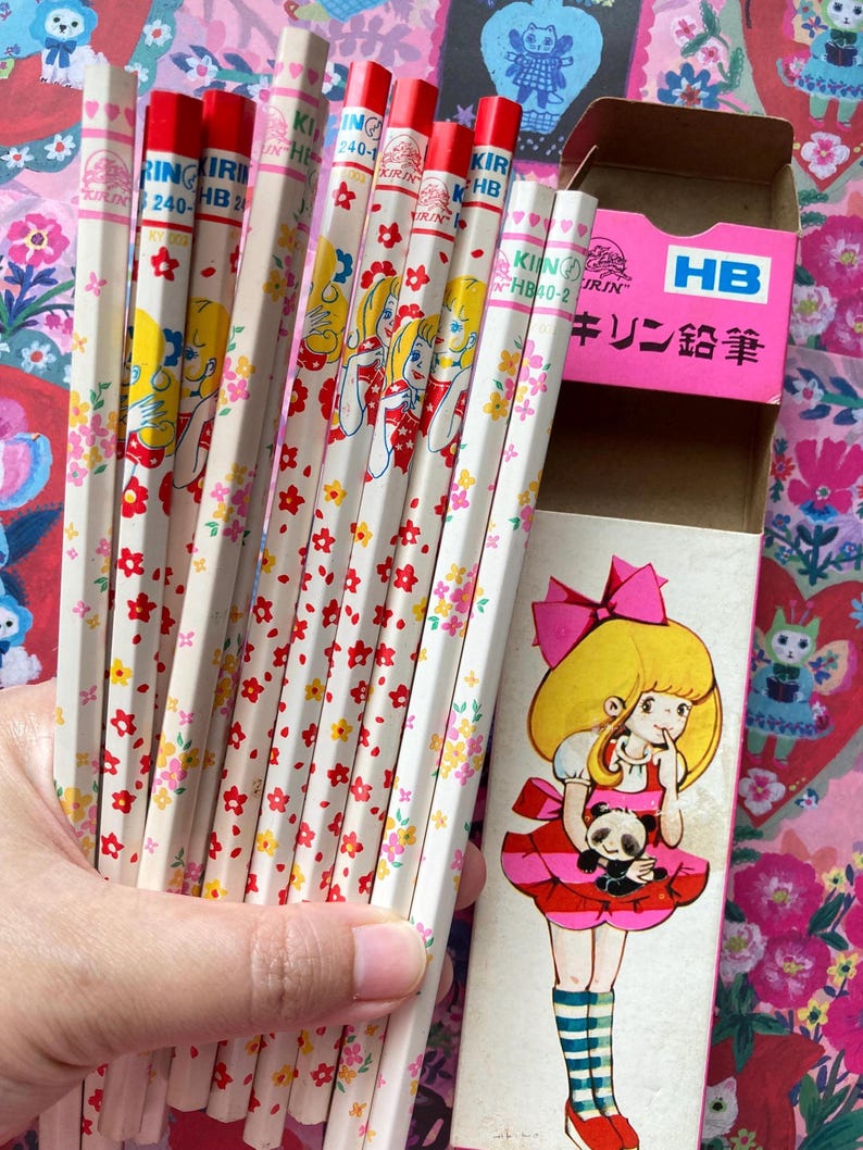 Puede incluir: Un conjunto de l&aacute;pices vintage con gomas rojas y barriles blancos decorados con dise&ntilde;os florales y de chicas de dibujos animados. Los l&aacute;pices est&aacute;n en una caja rosa con una ilustraci&oacute;n de dibujos animados de una ni&ntilde;a sosteniendo un panda.