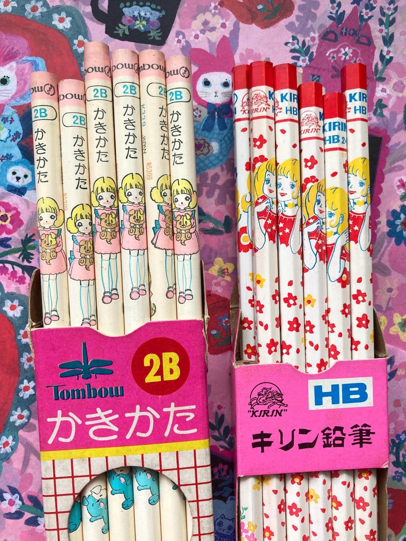 Puede incluir: Dos cajas de l&aacute;pices japoneses vintage. Una caja contiene l&aacute;pices con una ni&ntilde;a sosteniendo un oso de peluche, la otra con una ni&ntilde;a con un vestido rojo. Las cajas son rosas con texto japon&eacute;s y el grado del l&aacute;piz es 2B y HB.