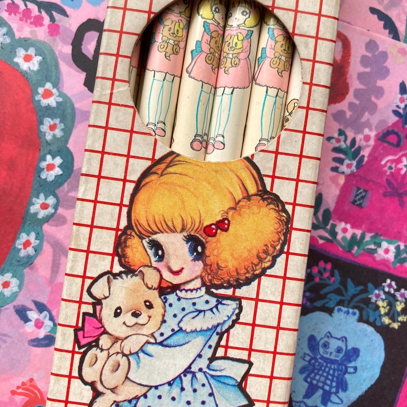 Puede incluir: Juego de l&aacute;pices vintage con una ni&ntilde;a de dibujos animados con un cachorro, con un vestido azul con lunares. La caja de l&aacute;pices tiene un patr&oacute;n de cuadr&iacute;cula roja y blanca. Los l&aacute;pices tienen un dise&ntilde;o de mu&ntilde;eca.