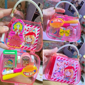 May include: Clear pink purse-shaped container with a white handle and gold accents. The container is filled with various small items, including a comb, pencil sharpener, and stationery. The container has a cartoon illustration on the front.