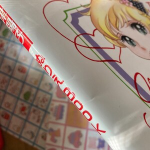 May include: A book cover featuring a manga-style illustration of a young woman with blonde hair and blue eyes. The cover has a white background with red and purple accents, and the word "Love" is written in a cursive font.