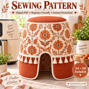 Puede incluir: Un patrón de costura para una funda de electrodoméstico de cocina con estampado floral en naranja quemado y blanco, parte superior naranja sólida y ribete de borlas color crema en el borde inferior. La funda tiene un corte en forma de U.
