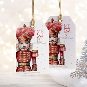 Puede incluir: Dos etiquetas de regalo de cascanueces rojas y doradas con las palabras "Feliz Navidad" y "Con amor, La familia Smith".