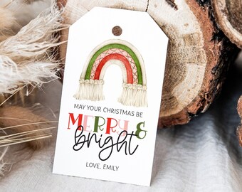 May include: A white rectangular gift tag with a hole at the top, featuring a watercolor illustration of a macrame-style rainbow in red, green, and beige. The text reads: MAY YOUR CHRISTMAS BE MERRY & BRIGHT, LOVE, EMILY. The design is clean and simple.