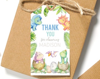 May include: A printable thank you tag with a dinosaur theme. The tag features a white background with green leaves, colorful dinosaurs, and the text "Thank You for showering Madison".
