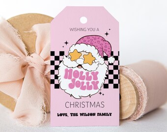Könnte beinhalten: Rosa-schwarzes Weihnachtsgeschenkanhänger mit einem Comic-Weihnachtsmann, der eine Sonnenbrille und einen Hut mit Leopardenmuster trägt. Das Etikett lautet "Wishing you a Holly Jolly Christmas, Love, The Wilson Family".