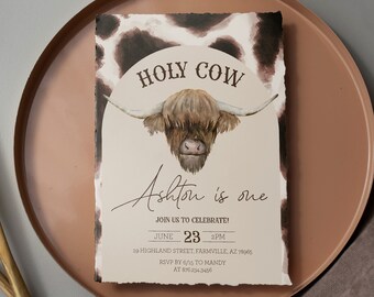 Puede incluir: Invitación imprimible y editable para una fiesta de primer cumpleaños con temática de vaca. La invitación presenta una ilustración de acuarela de una vaca Highland con el texto "Holy Cow Ashton is one" y los detalles de la fiesta.