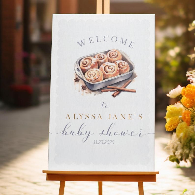 Może przedstawiać: Witamy znak na baby shower na sztaludze. Znak zawiera akwarelową ilustrację bułek cynamonowych w naczyniu do pieczenia, z tekstem "WELCOME to ALYSSA JANE'S baby shower 11.23.2025."
