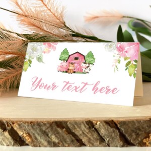 May include: A white folded card featuring a watercolour illustration of a red barn, a pig, a horse, and a cow, accented by pink and white floral arrangements. The text "Your text here" is printed in a pink cursive script on the front of the card.