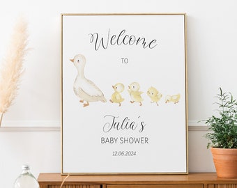 May include: A white sign with a gold frame featuring a watercolor illustration of a mother duck and her ducklings. The sign reads "Welcome to Julia's Baby Shower 12.06.2024".