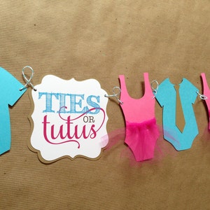 Pode incluir: Uma faixa de revela&ccedil;&atilde;o de g&ecirc;nero com recortes de papel azul e rosa de macac&otilde;es, uma gravata e um tutu. A faixa tamb&eacute;m inclui uma placa que diz "Ties or Tutus".