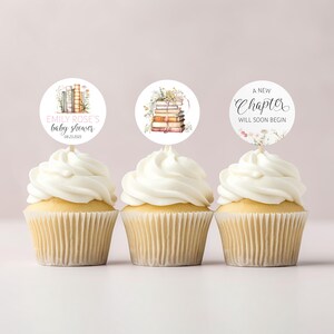 Peut inclure: Trois cupcakes avec un glaçage blanc surmontés de cercles de papier ronds. Les cercles sont illustrés de livres et de fleurs et portent le texte "Emily Rose's Baby Shower 08.22.2023" et "A New Chapter Will Soon Begin".