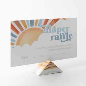 May include: A white card with a watercolor illustration of a sunset with a cloud and the text "diaper raffle". The card has a line for a name and the text "Please bring a pack of diapers in any size to be entered to win a prize".