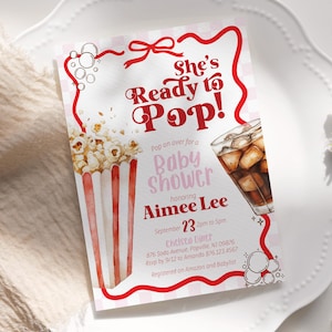 May include: Baby shower invitation with a popcorn and soda theme. The invitation features the text "She's Ready to Pop!" in red script, along with event details, including the honoree's name, date, time, and location. The design includes a watercolor illustration of popcorn and a glass of soda.