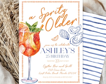 May include: A birthday invitation with the text "a Spritz Older" in orange script. The invitation features a watercolor illustration of a cocktail, oysters, and a slice of orange. The details include the name "Ashley's", the date, time, and location.