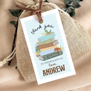 May include: A gift tag with a light blue scalloped border features the words "thank you" and "for celebrating with me!" A stack of books with a toy dinosaur and car are illustrated. The name "ANDREW" is printed at the bottom.