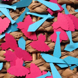 Pode incluir: Uma cole&ccedil;&atilde;o de recortes de papel azul e rosa em forma de gravatas e vestidos. Os recortes est&atilde;o espalhados sobre uma superf&iacute;cie tecida.