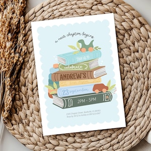 May include: A light blue invitation card with a scalloped edge, featuring a stack of illustrated books. The text "a new chapter begins" is at the top. The books have the text "JOIN US TO", "celebrate", "ANDREW'S", and "23 september". A toy car and dinosaur are on top.