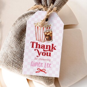 May include: A gift tag with a pink and white checkered pattern. The tag features illustrations of popcorn and a soda, with the words "Thank You" in red script. Below, it reads "for showering Aimee Lee" with a bow graphic.