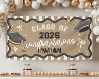Könnte beinhalten: Ein Abschlussbanner mit dem Text "CLASS OF 2026 congratulations HANNAH ANNE" in Schwarz und Weiß. Das Banner hat einen braunen Hintergrund mit einem wellenförmigen Rand und Abschlusskappen. Ballons und Desserts sind im Hintergrund.