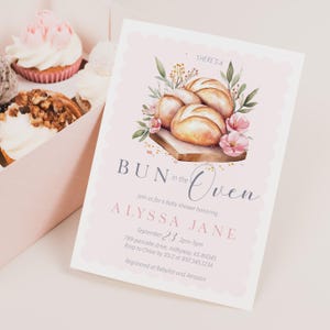 May include: A baby shower invitation with a watercolor illustration of bread rolls, flowers, and greenery. The invitation reads "BUN in the Oven" and includes details for Alyssa Jane's baby shower, including the date, time, and location.