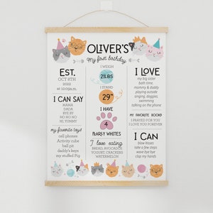 May include: A colorful printable poster with a cat theme celebrating a child's first birthday. The poster includes the child's name, Oliver, and details about their first year, including their weight, height, favorite foods, and things they can do. The poster is decorated with cute cartoon cats.