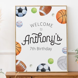 May include: A white sign with a gold frame featuring a watercolor illustration of various sports balls, including a basketball, baseball, football, soccer ball, and tennis ball. The sign reads "Welcome to Anthony's 7th Birthday".