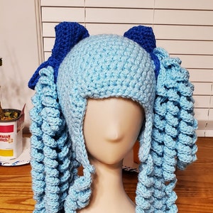 May include: A light blue crocheted hat with long, curly blue yarn strands. The hat has two blue bows on top.