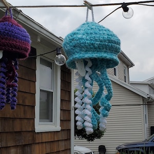 Puede incluir: Dos medusas de crochet colgando de un tendedero. Una es morada y la otra es azul y blanca.