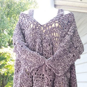 May include: A crocheted sweater with a loose, open-weave design. The sweater is made of a soft, fuzzy yarn in a light purple color. The sweater has a V-neck and a slightly cropped length.