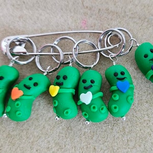Könnte beinhalten: Ein Set aus sechs grünen Gurken-Maschenmarkierern mit Herzen in verschiedenen Farben. Die Marker sind an einer silbernen Sicherheitsnadel und einem Ring befestigt.